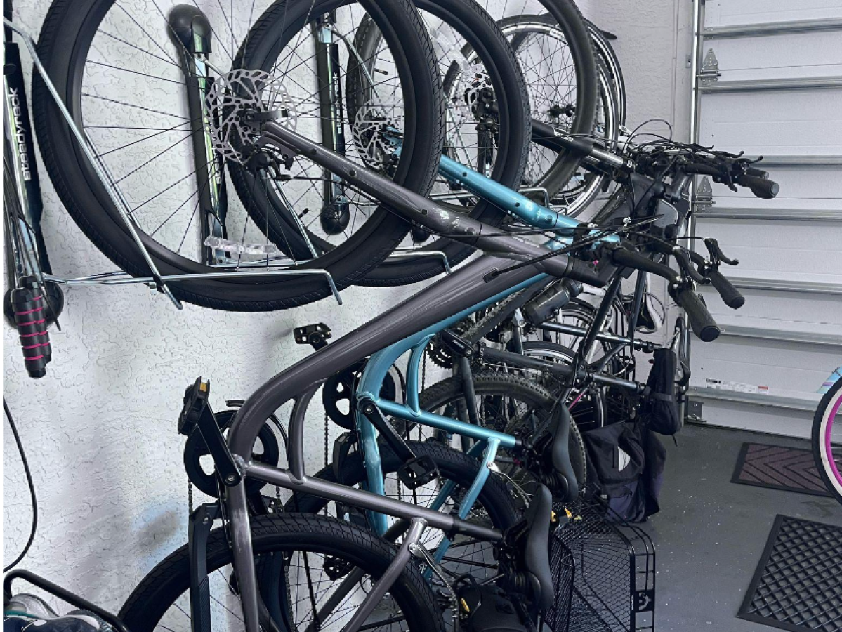 Five bicycles hanging vertically on a garage wall with a gray floor and closed garage door.