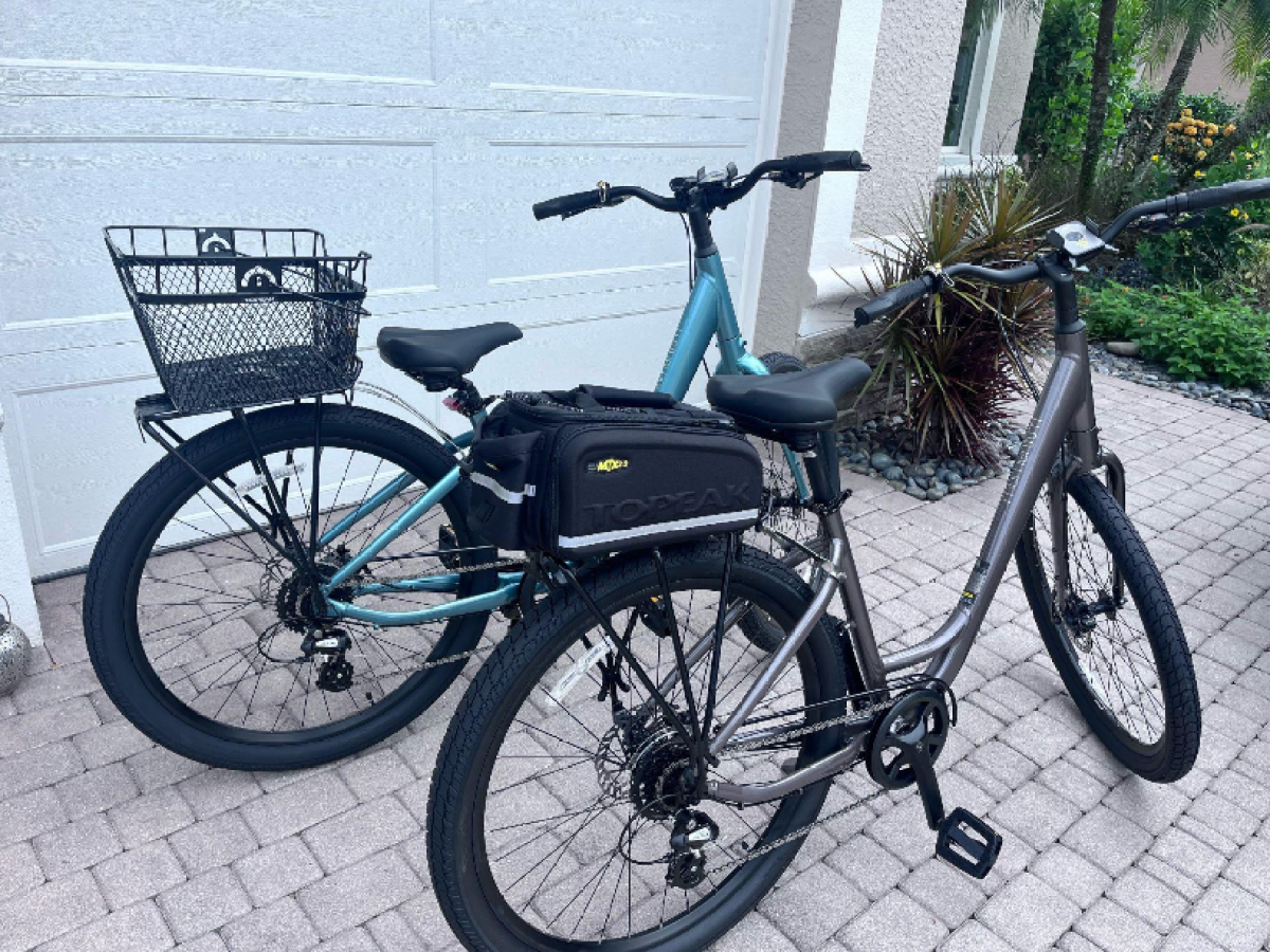 Two bicycles parked on a driveway, one with a rear basket, the other with a pannier bag.