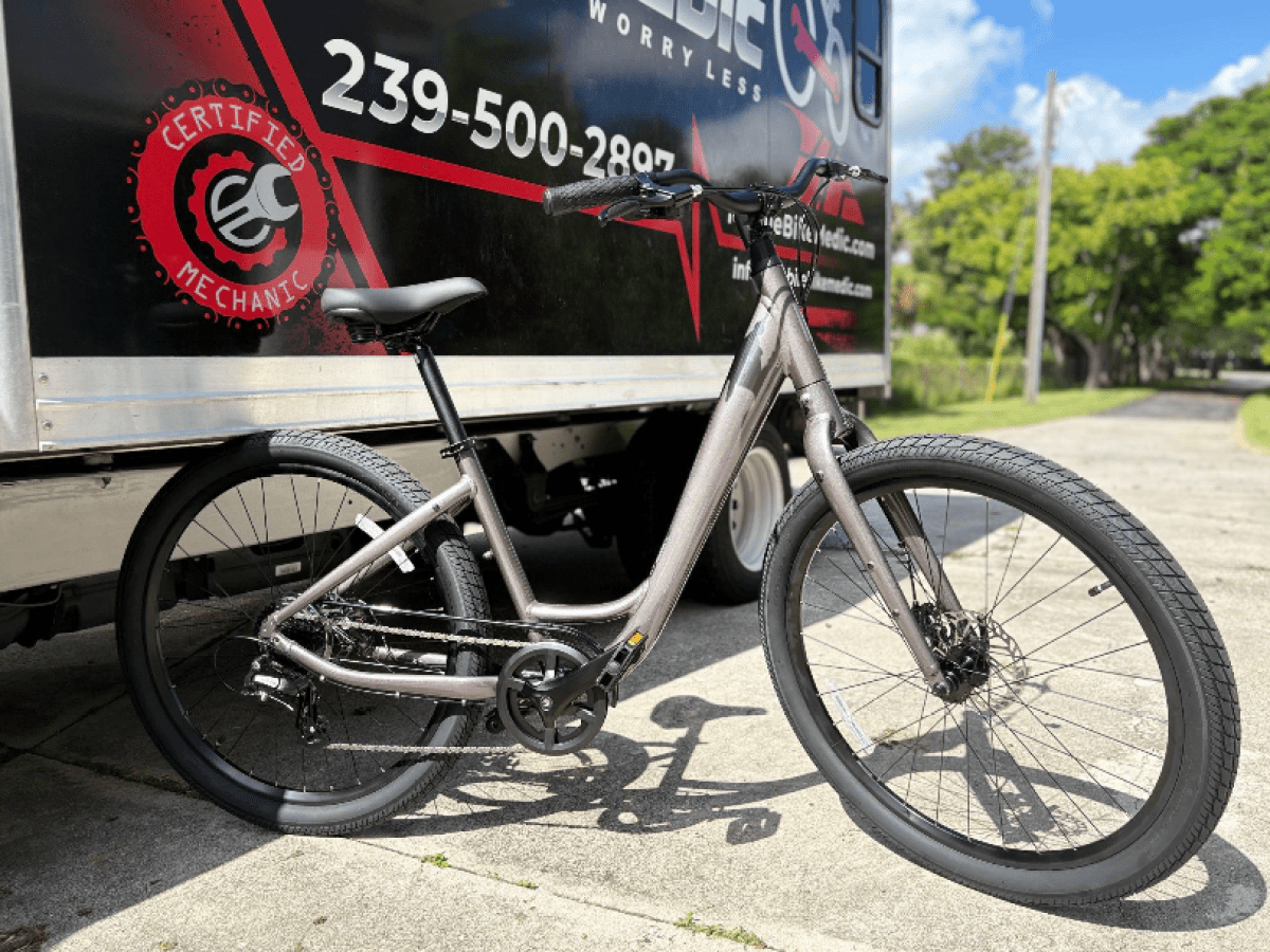 A gray bicycle parked beside a van with 'Certified Mechanic' logo and phone number.