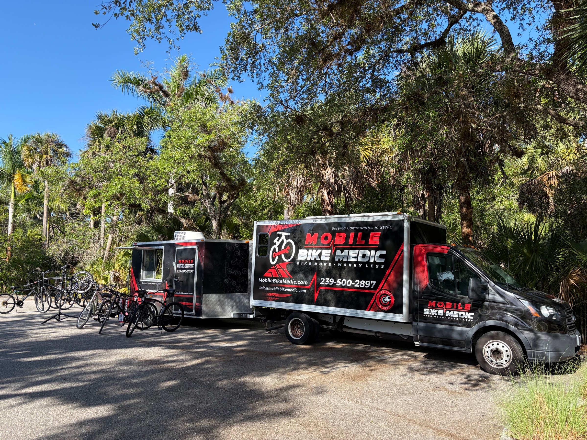 Mobile bike repair truck parked in a leafy area with bicycles nearby.
